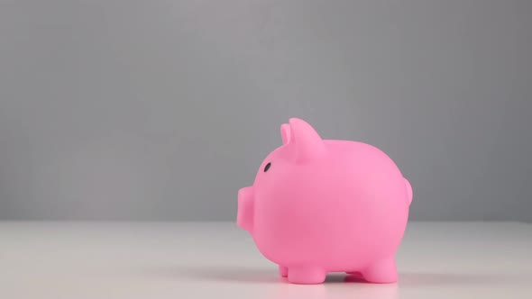 Faceless Caucasian Woman Folds a Small Heart Into a Pink Piggy Bank on a White Background