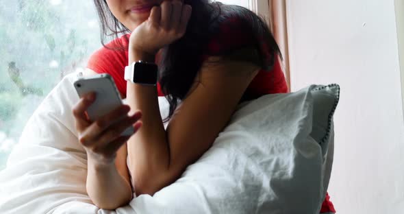 Happy woman using mobile phone in bedroom