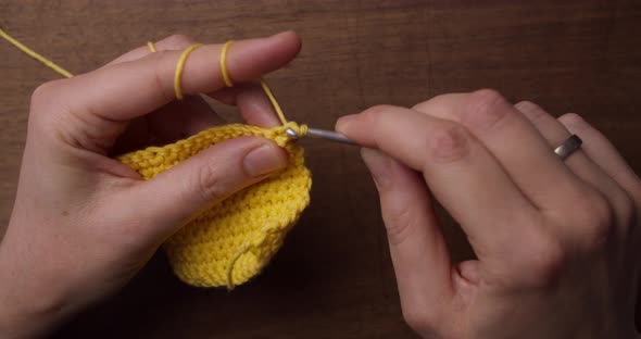 Top shot of a female holding a piece of yellow wool and a needle. Hands starting crocheting a yellow