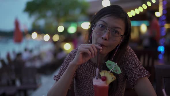 Asian Women Smiling While Drinking Cocktail At The Beach Restuarant With Light Bokeh At Night