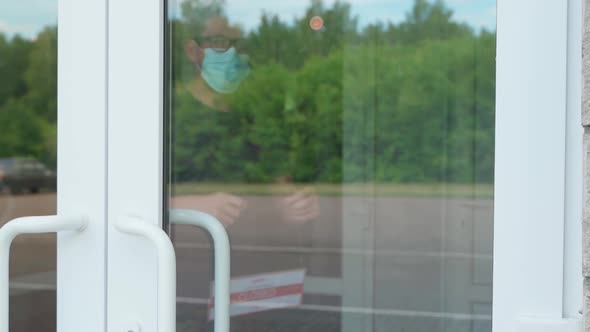 A Man Hangs a CLOSED Sign on a Transparent Door or Storefront During the COVID19 Pandemic