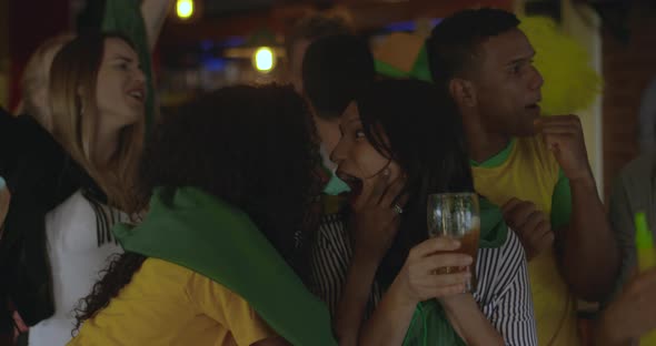 Brazilian football fans celebrating victory while watching match in sports bar, slow motion