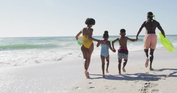 Smiling african american family holding hands and running on sunny beach