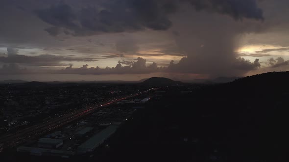 Aerial shot flying back of a highway leading to a hill with heavy clouds on the horizon