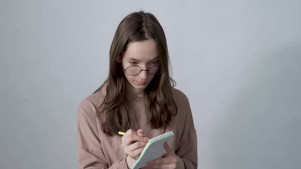 Young Inspired Woman Pensively Thinks and Making Notes in Paper Notebook