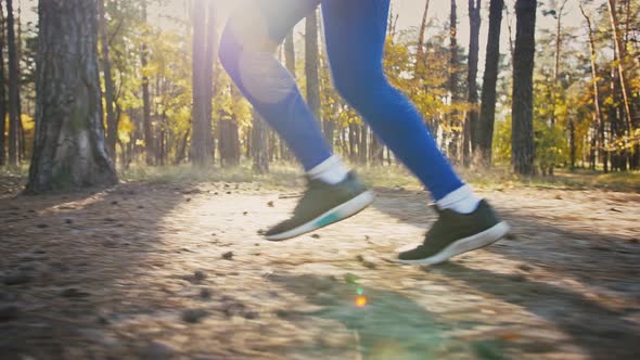 Legs of Unrecognizable Young Female Who Running By Path in Autumn Wood on Sunny Day