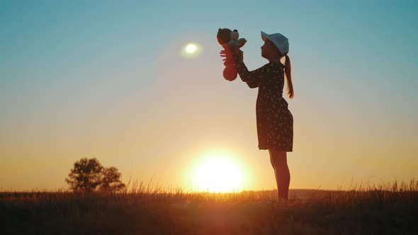 Little Girl in Dress Holding Teddy Bear Toy at Sunset. Silhouette of a Child with a Toy. Concept of