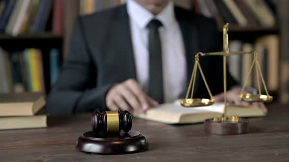 Close Up Shoot of Judge Hand Reading Book in Blur with Gavel and Scale 