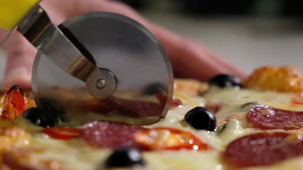 Baker cuts fresh hot pizza with cheese slices of pepperoni with a round knife