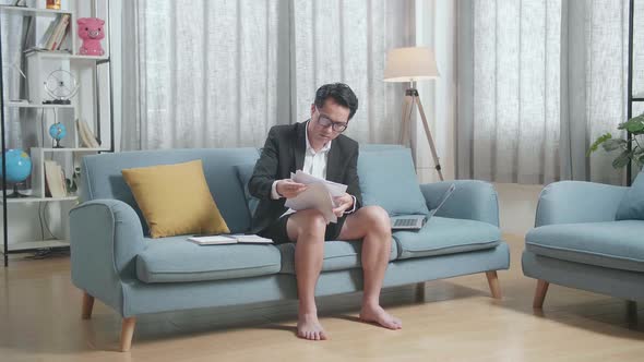 Full View Of Asian Businessman In Jacket And Shorts Checking The Documents While Working A Laptop