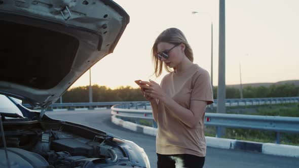 A Young Girl Stands on the Highway with a Broken Car Texting on the Phone. A Frustrated Girl Stands