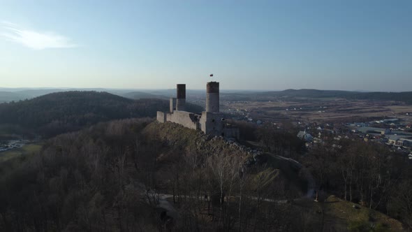 A rearward aerial drone shot of the Chęciny Royal Castle revealing all the landscape around it. This