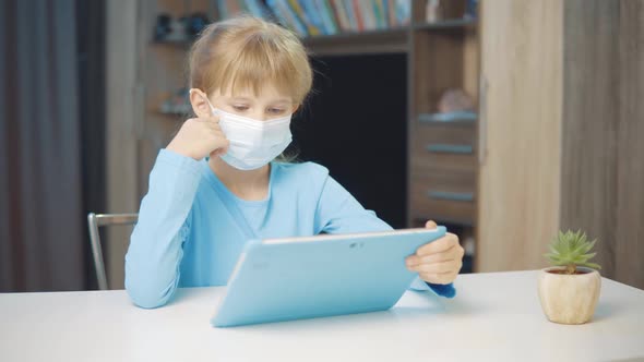 A 7Yearold Girl Wearing a Medical Mask Makes a Video Call on a Tablet