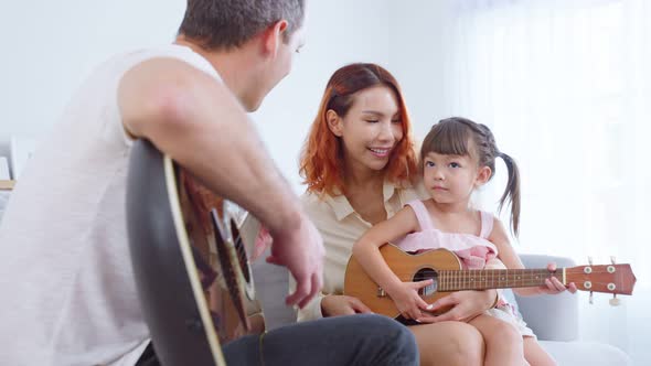 Asian young couple playing guitar with young baby kid together in living room in house.