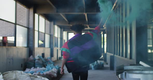 Mixed race man holding blue flare running through an empty building