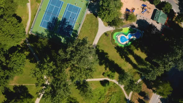 Scenic aerial view over tennis courts and playgrounds at a city park on a sunny, summer day.