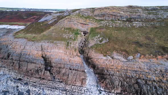 AERIAL: Pan out reveailing man made cave in the side of a cliff and rocky coastline, Culver Hole, Po
