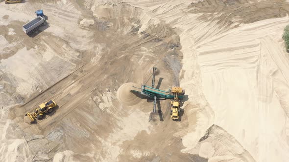 Top aerial view of bulldozer loading sand into empty dump truck in open air quarry.
