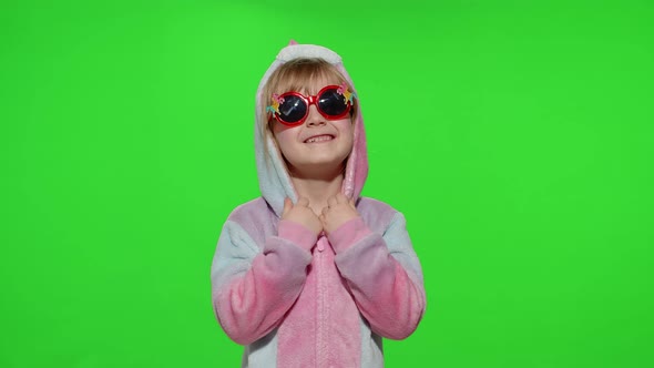 Little Blonde Child Girl Smiling Puts on Sunglasses in Unicorn Pajamas Costume on Chroma Key