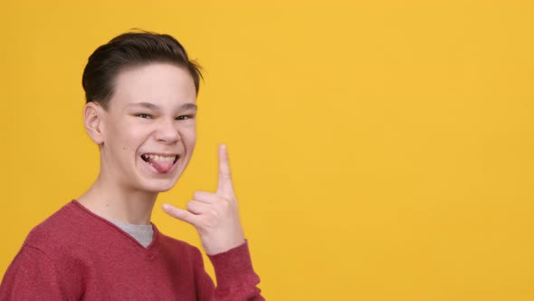 Funny Teen Boy Gesturing Rock Sign Showing Tongue Yellow Background