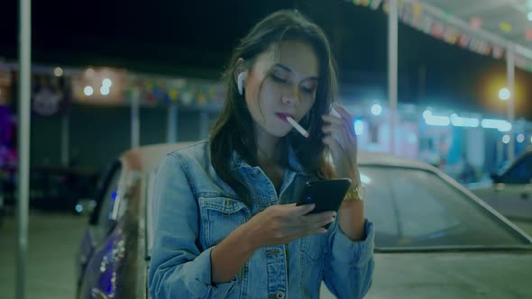 A Girl Smokes in Front of a Rusty Classic Car While Typing a Message Late at Night