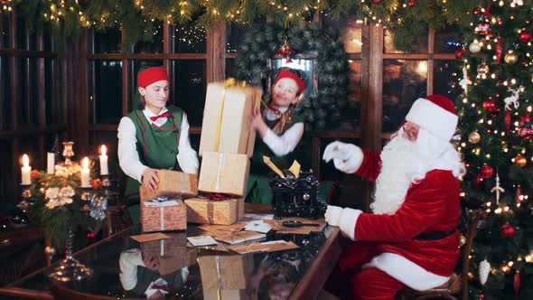 Christmas elves stack New Year's gifts on a Santa Claus table in a room