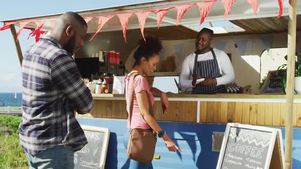 Smiling african american male food truck owner taking order from woman, and man waiting in queue