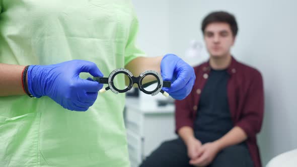 Closeup Optometry Trial Glasses in Hands of Unrecognizable Ophthalmologist with Blurred Patient