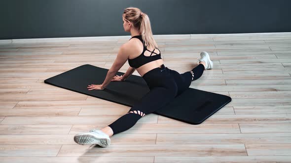 Sportswoman Doing Push Ups Sitting in Twine on Mat Training at Modern Gym