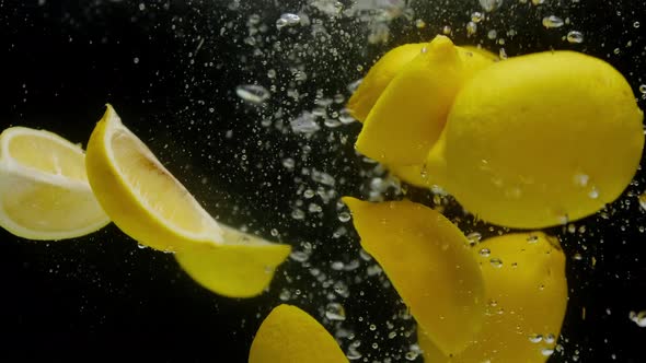 Closeup of Falling Sliced Lemons Into the Sparkling Water on Black Background Making a Cocktail of