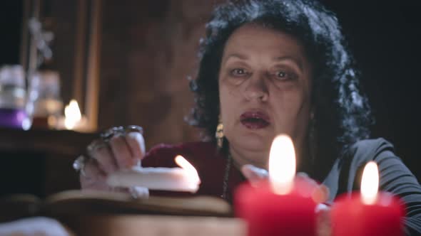 Middle-aged Female Psychic Holds Burning Candle Over Bowl with Water