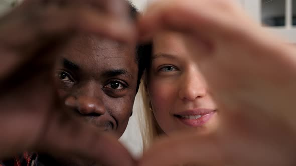 Close Up Smiling Multiethnic Couple Faces Looking Through Joined Fingers Heart