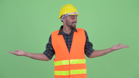 Happy Young Bearded Persian Man Construction Worker Comparing Something