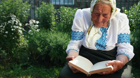 An Old Grandmother is Sitting on the Street and Reading a Book
