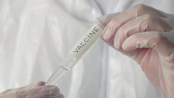 Virologist Holding Tube with Vaccine Inscription in Scientific Laboratory. Transparent Liquid in