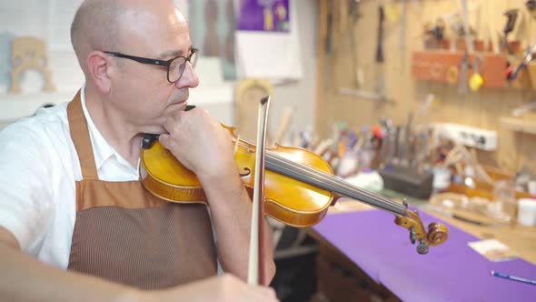 Luthier master playing violin in workshop