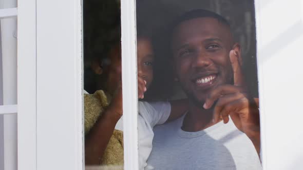 African american daughter holding teddy bear looking through window with her father