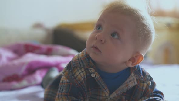 Little Boy in Soft Shirt Lies on Comfortable Bed in Room