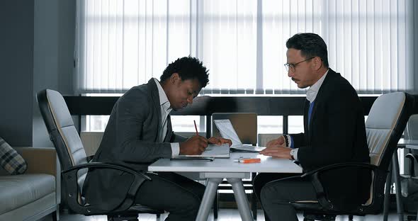 Two Young Businessman Talking at Desk in Office