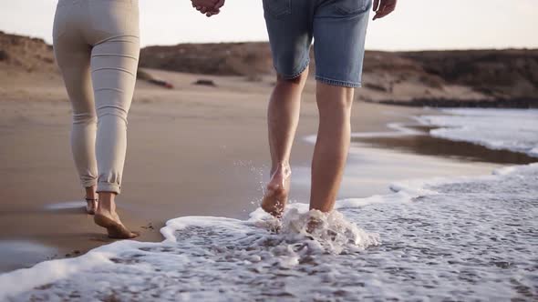 Unrecognizable Young Couple Stepping Together at the Golden Sand at Sea Beach