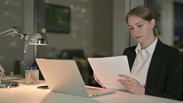 Ambitious Businesswoman Reading Document on Office Desk at Night