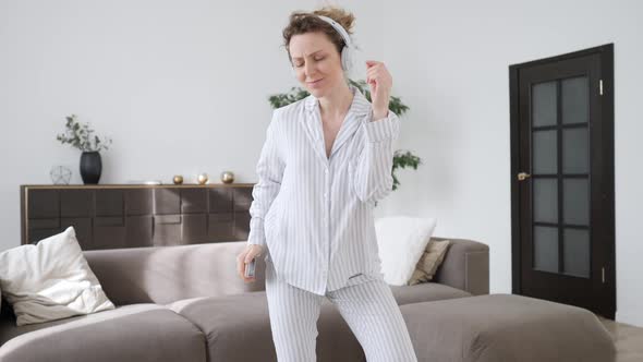 Young Happy Woman Listening Music In Headphones With Smartphone And Dancing In Living-Room