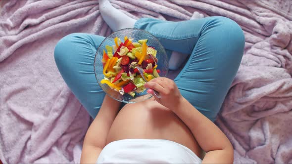 A Pregnant Girl with a Large Bare Stomach Mixes Vegetable Salad and Eats Sweet Peppers, Top View