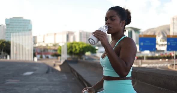 Fit african girl drinking water after sport workout with city in background