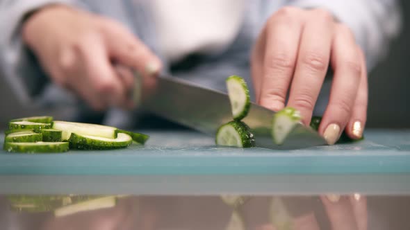 Front View of Woman's Hands Slicing Fresh Cucumber on Cutting Board in Slow Motion