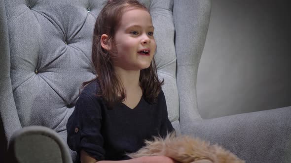 Adorable Girl Is Playing with a Small Puppy on Chair