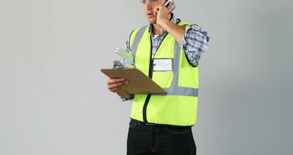 Male architect holding clipboard and talking on mobile phone