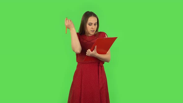 Tender Girl in Red Dress Fills Papers in Red Folder with Pensil. Green Screen