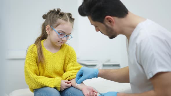 Portrait of Concentrated Scared Girl Sitting on Medical Couch As Blurred Doctor Disinfecting Hand