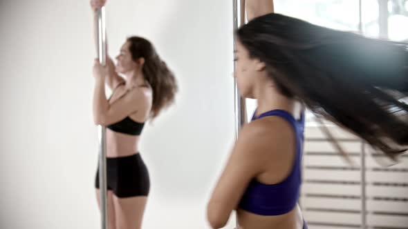 Two Sportive Women Having a Pole Dancing Training in the White Studio